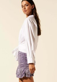 Chemise blanche à boutons, avec des manches bouffantes, associée à une jupe violette en sequins, froncée avec des volants au bas.