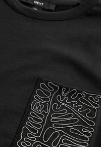 T-shirt nera con tasca testurizzata e un design a linee argentate e ondulate. Realizzata in cotone, ha un collo rotondo e maniche corte.