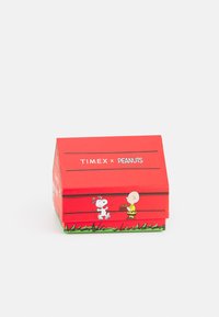 Boîte en carton rouge avec un toit incliné. Illustrations de Snoopy et Charlie Brown. Le texte indique "TIMEX x PEANUTS." Accent de pelouse verte.