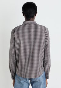 Long-sleeve shirt with a checkered pattern in shades of red and navy, made from a lightweight fabric; features a standard collar and button cuffs.