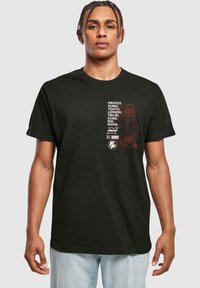 Sort bomulds t-shirt med grafisk tekst i hvid og rød, der viser bynavne og et stiliseret bildesign på fronten.