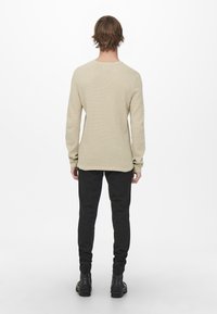 Beżowa, teksturowana koszula z długim rękawem, z okrągłym dekoltem i luźnym krojem, zestawiona z czarnymi spodniami o wąskim kroju i botkami za kostkę.