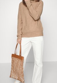Beiger, strukturierten Pullover mit hohem Kragen, kombiniert mit weißen, weiten Hosen. Eine braune Netztasche mit Ledergriffen.