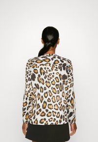 Blusa con stampa leopardata, maniche lunghe, realizzata in tessuto morbido, con una base bianca e macchie nere e marrone dorato, orlo arrotondato.