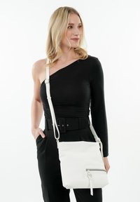 Bolso cruzado de piel blanca con forma cuadrada, herrajes plateados y un bolsillo frontal con cremallera. Correa ajustable. Acabado texturizado.