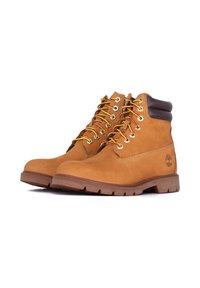Une paire de bottes de travail en cuir beige avec des cols rembourrés marron foncé et des lacets jaunes, présentée sur fond blanc.