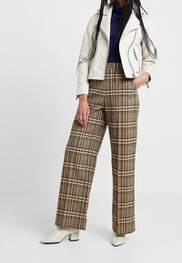 Bílá kožená zkrácená motorkářská bunda, námořnický rolák, hnědé kostkované široké kalhoty a bílé kotníkové boty s blokovým podpatkem.