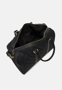 Borsa duffle trapuntata nera con accessori dorati, zip superiore, due manici e tracolla regolabile. Interno in tessuto nero, spazioso.