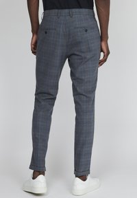 Šedé kalhoty s károvaným vzorem a střih na míru, s poutky na pásek, dvěma zadními kapsami s knoflíky a ohrnutými lemy, doplněné bílými teniskami.