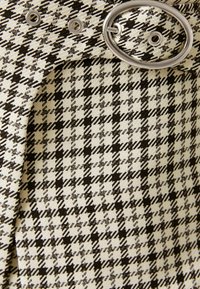 Schwarz-weißes Hahnentristoff mit einer gewebten Textur, ausgestattet mit einer silbernen ovalen Schnalle und Ösen. Das Design zeigt ein strukturiertes, kariertes Muster.