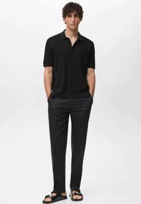 Polo shirt nero a maniche corte con una texture sottile, abbinato a pantaloni scuri su misura e sandali neri con un accent decorativo.