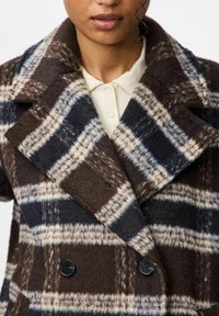 Cappotto in lana doppiopetto in motivo tartan marrone e blu navy. Presenta ampie rever, tessuto testurizzato e bottoni neri. Il colletto si adatta vicino al collo.