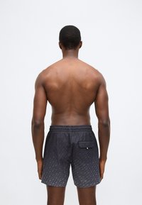 Črne kopalne hlače z vtisnjenim vzorcem, elastičnim pasom in zadnjim žepom. Gladek material z mat zaključkom.