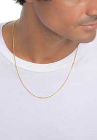 Collana a catena in tonalità oro con design intrecciato, appoggiata su una t-shirt bianca con collo rotondo, che mostra una texture metallica liscia.