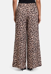 Pantalons larges imprimés léopard en beige et noir, avec une texture douce et une taille élastique pour plus de confort. Design à ourlet ouvert.