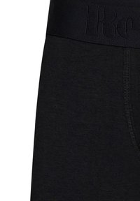 Schwarz gefittete Unterwäsche mit einem strukturierten, elastischen Bund, der ein erhabenes Logo trägt. Glatte Spitze und saubere Nähte entlang der Säume.