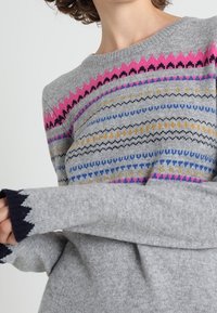 Gestrickter grauer Pullover mit Rundhalsausschnitt, der bunte geometrische Muster in Pink, Blau, Gelb und Schwarz auf der Brust und den Ärmeln zeigt.