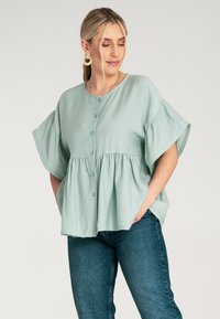 Jasnozielona bluzka zapinana na guziki z krótkimi, falbanowymi rękawami i szwem w talii. Wykonana z miękkiego materiału, o luźnym kroju i delikatnej fakturze.