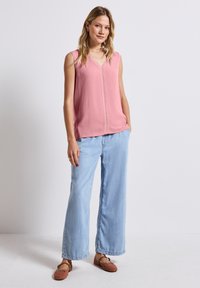 Blouse sans manches rose avec décolleté en V, présentant des détails verticaux, associée à un jean large bleu clair et des ballerines blush. Design simple, texture douce.