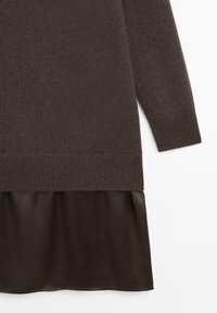Ciemnobrązowy, długi sweter z dzianiny z prążkowanymi mankietami i dołem, noszony na warstwie dopasowanej brązowej spódnicy z satyny.