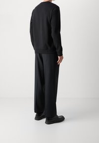 Černá mikina s kulatým výstřihem a žebrovanými manžetami, ve spojení s černými kalhotami širokých nohavic a černými botami. Hladká textura, minimalistický design.