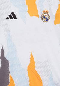 Biely futbalový dres so abstraktnými vzormi v sivej, modrej a oranžovej farbe. Obsahuje čierne logo Adidas a vyšívaný znak Real Madrid.