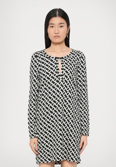 Robe à manches longues noire et blanche avec un motif géométrique en chaîne, un col rond avec un détail en forme de trou de serrure, et une coupe décontractée.