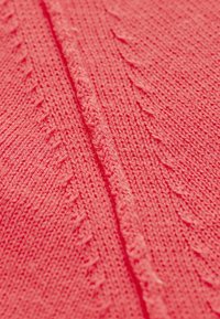 Gros plan sur un tissu en tricot rose avec une couture centrale et des motifs diagonaux texturés le long des bords.
