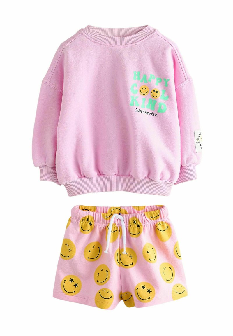 Rosa sweatshirt med grön text och smiley-grafik, ihopparad med rosa shorts som har mönster av gula smiley-ansikten, med elastisk midja.