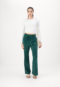 Un pantalon en velours côtelé vert avec des côtes verticales, associé à un haut ajusté à manches longues blanc. Les accessoires incluent un sac à main léger.