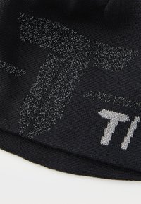 Svart strikket lue med teksturert, reflekterende grafisk design i sølv, med fremtredende bokstaver og abstrakte former over hele stoffet.