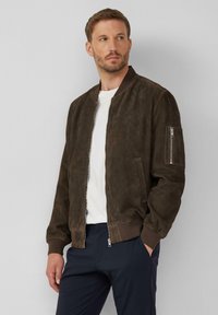 Braune Wildleder-Bomberjacke mit gerippten Bündchen und Saum, Reißverschlusstasche am Ärmel und zwei Seitentaschen. Kombiniert mit einem weißen T-Shirt und dunklen Hosen.