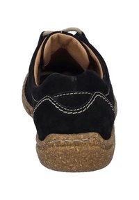 Chaussure en suède noir avec une semelle texturée marron, ornée de coutures blanches et d'une forme arrondie. L'intérieur est beige.