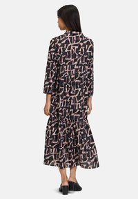 Langes schwarzes Kleid mit einem gestuften Rock, der ein geometrisches Muster in Pink und Weiß aufweist. Hergestellt aus leichtem Stoff, mit 3/4-Ärmeln und einem Kragen.