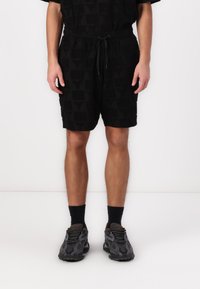 Black shorts with a textured pattern, elastic waistband with drawstring, and side pockets. Worn with black socks and textured black sneakers.