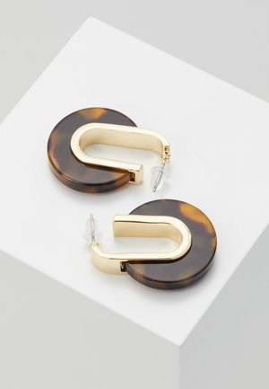 Kullanväriset korvarenkaat tummilla kilpikonnakuviolisillä ja kirkkailla muovitaustoilla valkoisella pinnalla.