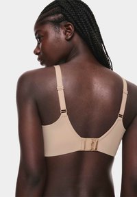 Reggiseno beige con spalline regolabili, texture liscia e chiusura a gancio e occhiello sul retro. Design semplice senza decorazioni.