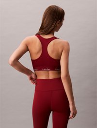 Sutien sport burgundy cu design racerback, având o bandă elastică cu marcă. Asortat cu colanți cu talie înaltă, cu textură netedă.