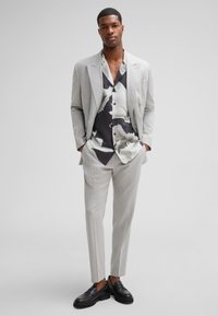 Jasnoszary garnitur z wyciętymi klapami, połączony z czarno-białą koszulą w kwiaty. Czarne półbuty dopełniają stylizację. Gładka tkanina, dopasowany krój.