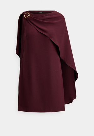 Burgunderrotes knielanges Kleid mit einem drapierten Umhangdetail, das mit einer goldenen Schnalle an einer Schulter befestigt ist, vor weißem Hintergrund.