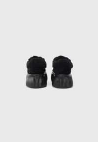 Chaussures noires avec une semelle texturée et nervurée. La tige est en matériau doux et moelleux, avec un design arrondi et un style minimaliste.