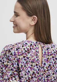 Floral blouse featuring a light fabric with purple, black, and brown flowers on a white background. Includes a keyhole detail at the back.