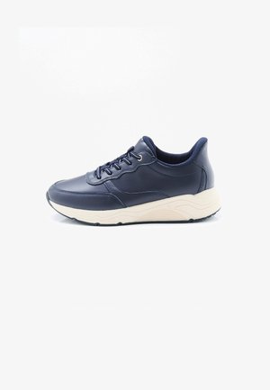 Zapatilla deportiva de cuero azul marino con suela blanca gruesa y cordones negros, mostrada de lado sobre un fondo blanco.