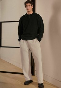 Sort fleece-pullover med krave og to knapper, parret med lysegrå, løstsiddende sweatpants og sorte sneakers.