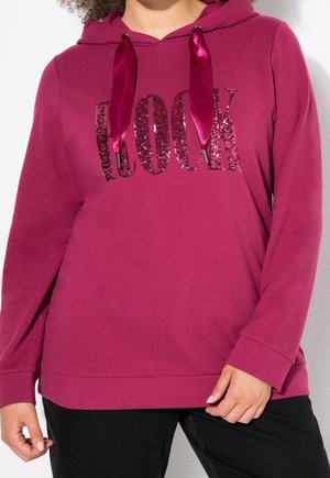 Personne portant un sweat à capuche rose foncé avec des cordons brillants et des lettres en sequins épelant "ROCK" sur la poitrine.
