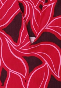 Tissu rouge avec un motif floral abstrait noir et rose et une petite ouverture en forme de V au niveau du col.