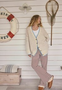Preveliki kremasti kardigan s plavim obrubom, drvenim gumbima i zvonolike hlače crveno-bijelih pruga. Meka tekstura, ležeran dizajn.