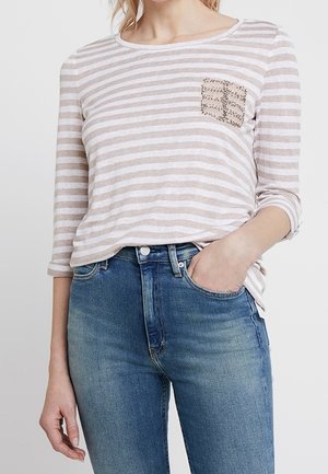 Ljust beige och vit randig långärmad skjorta med en paljettficka, tillsammans med högmidjade blå denimjeans.