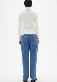 Weißes, geripptes Rollkragenshirt und lässige, hell gewaschene blaue Jeans mit zwei Gesäßtaschen und geraden Beinen.
