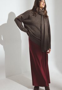 Brauner übergroßer Pullover mit geripptem Saum, kombiniert mit einem langen burgunderfarbenen Rock. Enthält einen passenden Schal mit durchgehend weichen Texturen.